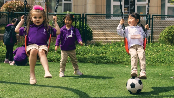 三名女学生在烟台华盛国际学校幼儿中心外踢足球和荡秋千