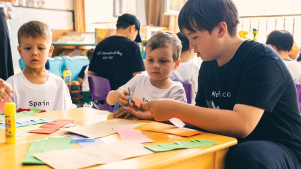 烟台华盛国际学校幼儿中心内，三名男学生正在剪彩纸