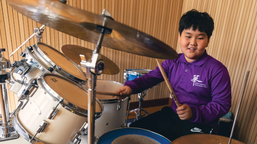 烟台华盛国际学校内，一名年轻的男学生正在学习打鼓