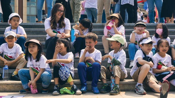many young students at yantai huasheng international school learning outside on the steps with their teacher
